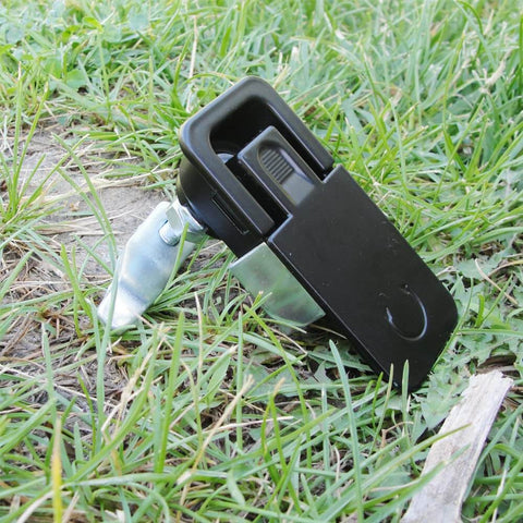 Two piece compression latch with flush sealed lever, lift and turn adjustable grip in black, placed on grass.