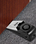 Black Door Stop Alarm with 120DB Siren for Home & Travel installed under wooden door on carpet
