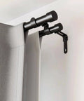 Black double curtain rod with wall brackets, holding gray curtains in a living room setting.