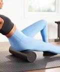 Woman using High Density 12 Inch Foam Roller for Exercise and Recovery in Black on yoga mat for flexibility training.