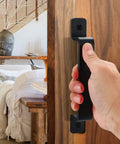 Hand gripping 7.4 inch black sliding barn door handle installed on wood surface, highlighting durable metal pull design for indoor use.