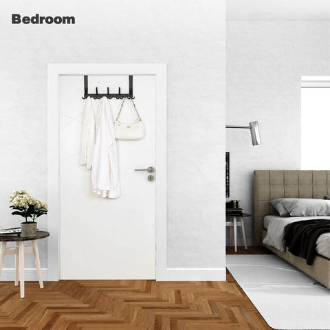 Over the Door Towel Rack with 15 Triple Hooks Black Metal in a bedroom, holding a bag and coats on a white door.