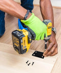 Installation of a black metal flat straight brace bracket, 2.4 x 1.5 inch, on wooden surface using a drill and screws.