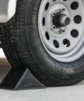 Beefy Rubber Wheel Chock For Cars Trailers RVs And Utility Vehicles With Reinforced Grip Weather And Chemical Resistant 5x6x5 Inch Tire Stopper For Secure Parking And Service Bays Buyers Products WC1467A installed on vehicle tire.
