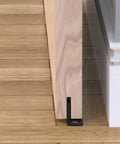 Sliding Barn Door Floor Guides Black 4 Pack Bottom Track Guides For All Sliding Doors Including Bypass And Pocket Doors Easy To Install Closet And Barn Style Durable Plastic Guides For Grooved And Non Grooved Tracks installed on wood floor with door.