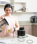 Woman in kitchen with blender, two gray rubber seals for 2 Pack Blender Gasket O-Ring Replacement For Oster Osterizer Blenders.
