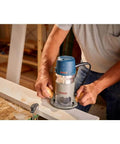 Person using Bosch 1617EVSPK Combo Router with plunge and fixed base, 2.25 HP motor, for woodworking on a table.
