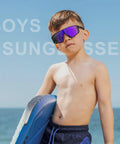 Boy wearing UV400 sunglasses at the beach, part of Three Pack Kids Sunglasses UV400 For Ages 6 To 14 Black Blue White.