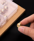 Close-up of hand holding a brass ball from Precision Brass Bearing Balls Set 120-Piece Assortment 3/32 To 1/2 Inch Sizes with storage box.