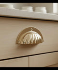 Installed brass cup handle with elegant scalloped shell design on kitchen cabinet drawer for easy gripping