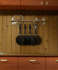 Wall-mounted bronze pot rack with 4 black frying pans hanging on double bars against a wooden wall, highlighting kitchen organization.