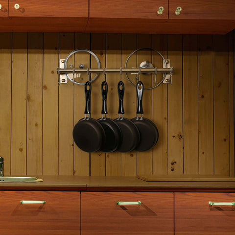 Wall-mounted bronze pot rack with 4 black frying pans hanging on double bars against a wooden wall, highlighting kitchen organization.