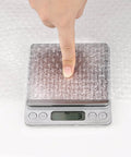 Finger pressing down on 2 Pack 12 Inch Bubble Packing Wrap 72 Feet Perforated Every 12 Inches for Moving Boxes and Shipping Cushioning