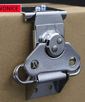 Close-up of a small butterfly twist latch with keeper plate in zinc plated steel, installed on a cardboard surface for secure closure.