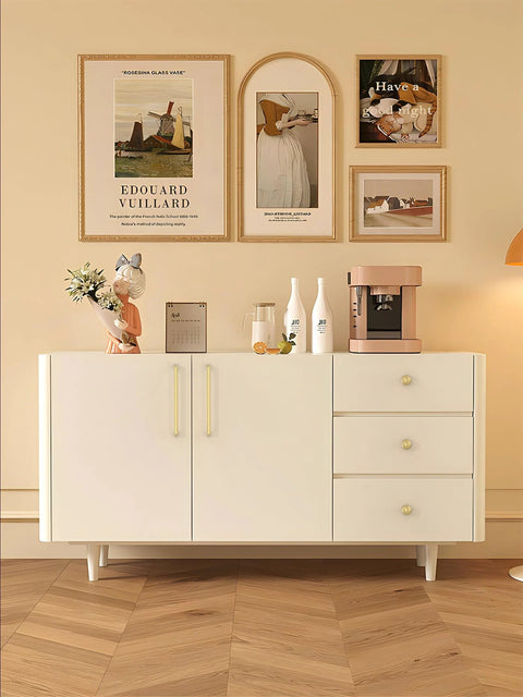 Stylish sideboard decorated with framed art, ceramic vases, and a coffee maker on top, set against a beige wall and wooden floor.