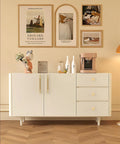 Modern white sideboard with decorations and artwork on wall, including a bronze-colored coffee machine.
