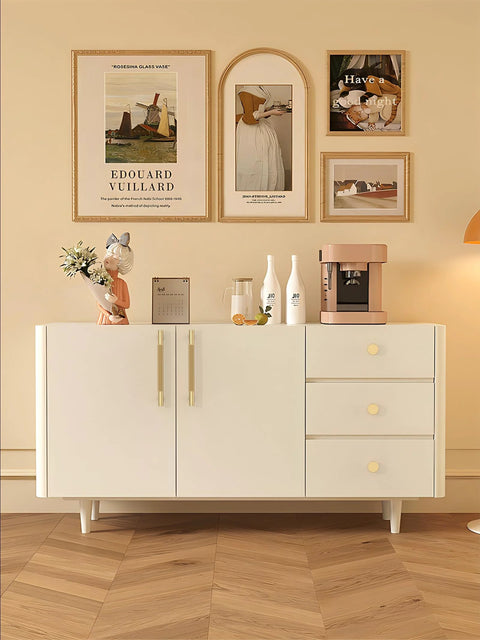 Modern white sideboard with decorations and artwork on wall, including a bronze-colored coffee machine.