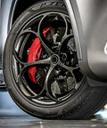 Close-up of a car wheel with a tire featuring a red brake caliper and rim, highlighting performance features.