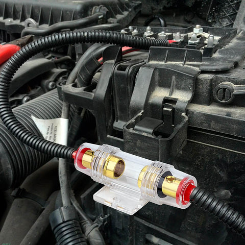 Dual Fuse Holder Kit With 100A AGU Fuses installed in car engine bay, clear polycarbonate body, gold plated terminals, 4-8 AWG wire compatible.