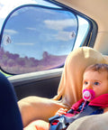 Baby with pacifier sitting in car, protected by transparent PVC sunshade on window