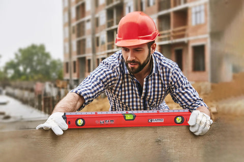 Worker using 24 inch box level with three durable acrylic vials, precise 1/16 inch ruler, wall grip, hand calibrated straightedge on site.
