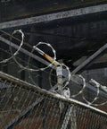 Barbed wire on chain link fence with industrial background, featuring 5" Pipe Track Wheel Galvanized, 1 7/8" Round Post for gate frame.