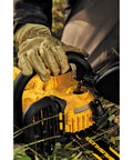 Person filling yellow chainsaw with oil outdoors, wearing gloves, showing durable construction of tool