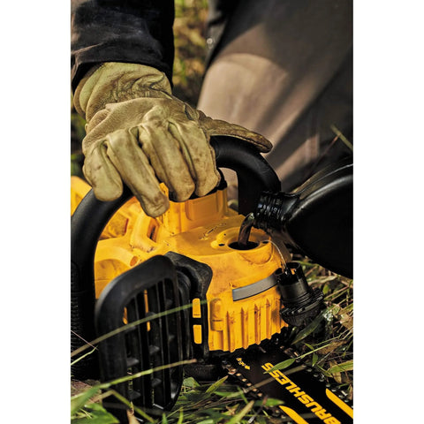 Person filling yellow chainsaw with oil outdoors, wearing gloves, showing durable construction of tool