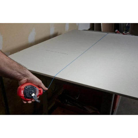Milwaukee Chalk Line Reel Set F in use, showing 100 ft blue line marking a board for precise layout on construction project.