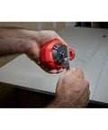 Person holding Milwaukee Chalk Line Reel Set F with 100 ft blue line, drawing layout mark on grey surface.