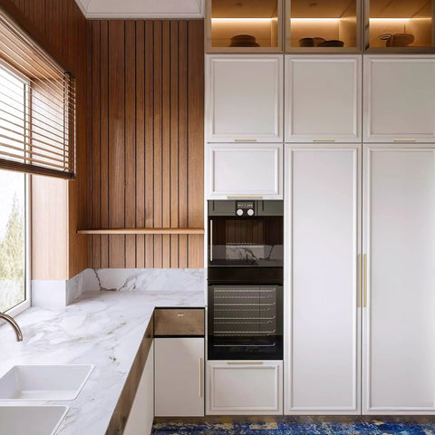 Modern kitchen with champagne bronze cabinet handles, featuring stainless steel pulls on white cabinets against a wood-paneled wall.