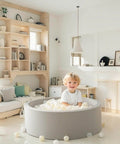 Child playing in a grey indoor ball pit with Ball Pit Balls Plastic Playballs for Baby Toddlers Kids Boys Girls Playhouse Decor Play Pool Fun Phthalate-Free BPA-Free Bath Toy White Beige Transparent,100 Balls in a cozy living room.