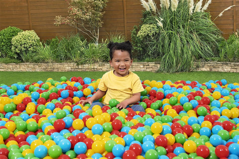 Child playing in Play Balls 100ct set, colorful plastic balls for indoor play, ball pits, and bouncers, in a garden setting