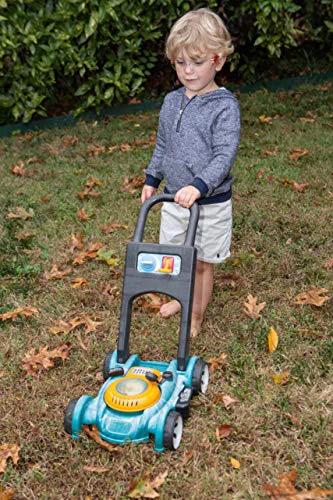 Young boy playing with toy lawnmower on grass.