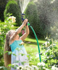 Child watering garden with hose, using sprinkler nozzle.