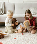 Two children playing with stuffed animals on a beige textured rug in a cozy living room setting.