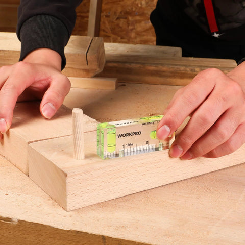 Hand using compact magnetic 3 inch mini level with two bubbles to align wooden surface showcasing shatterproof construction.