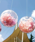 20 Pack 4-Inch Clear Plastic Fillable Ornaments Ball, hanging outside with pink flowers inside, ideal for Christmas, wedding decor.