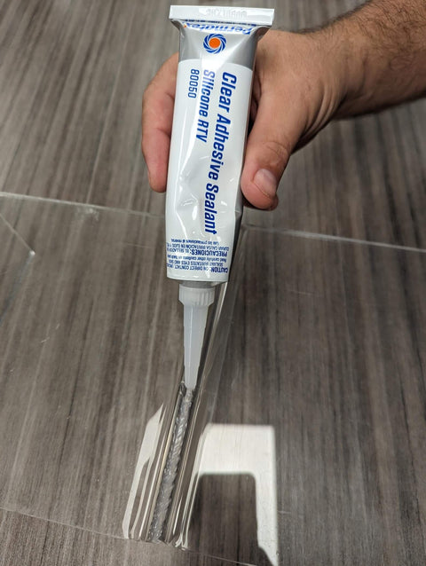 Applying Clear RTV Silicone Adhesive Sealant, 3 Oz Tube, Pack Of 12, onto glass surface for sealing and bonding purposes.