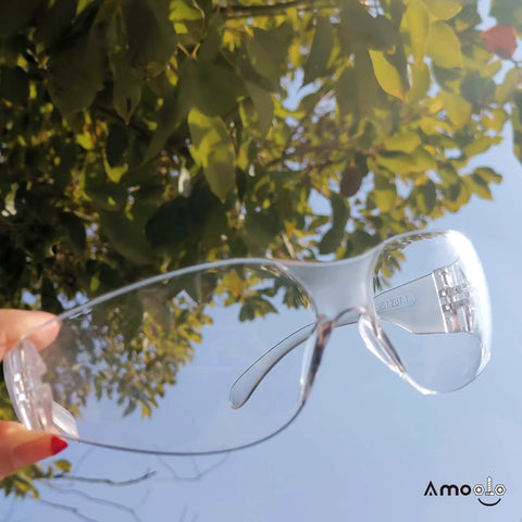 Person holding Clear Safety Glasses 24 Pack ANSI Z87.1 Impact Resistant Eye Protection UV400 against blue sky backdrop