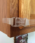 Clear self adhesive safety latches on wooden cabinet corner for childproofing, 9-inch length, no tools required, with four flaps.