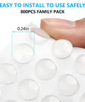 Close-up of 800 Pack Clear Cabinet Door Bumpers Self Adhesive Cushions for Cabinets, Drawers, Frames and Furniture No Hassle Quiet Close Invisible 0.24 Inch Silicone Stoppers for Noise Reduction and Surface Protection on fingertip, showing self-adhesive backing and 0.24 inch size.