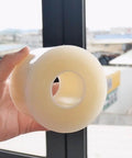 Hand holding Window Weather Sealing Tape, 3 Inch x 165 FT(55 Yards), clear roll near a window