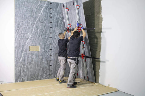 Two workers installing a large tile using handling tools with Slim Easy Trans Supplementary Guide Set Perpendicular Guides for Increased Stability.