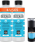 Two Pack Universal Coffee Descaler For All Machines Including Keurig Nespresso Delonghi And Other Single Serve Coffee And Espresso Makers Made In USA 8 Oz Bottles Providing Four Descale Sessions To Remove Mineral Buildup And Residue next to coffee maker with cup.