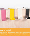 Colorful over the door hooks in pink, yellow, white, and silver, shown installed on a wooden door. Easy to install design.