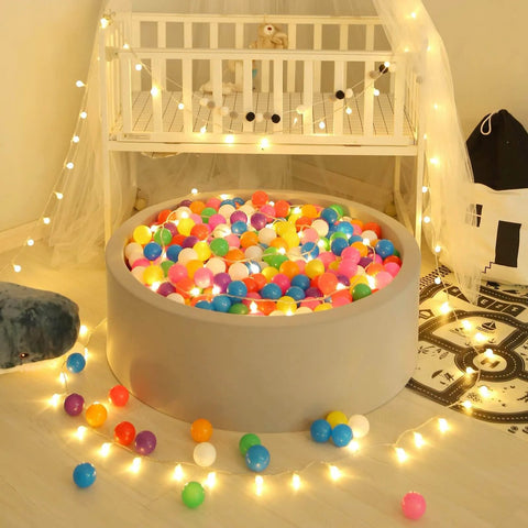Ball Pit Balls for Toddles Kids Plastic Ballpits Accessories Crush Proof Durable Fun Shape Play Baby Bath Toys,2.15inch 100count Mix Color in a gray ball pit surrounded by string lights.