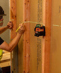 Compact self-leveling laser level with bright green cross lines and 360-degree planes in use on construction site