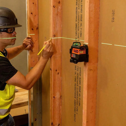 Compact self-leveling laser level with bright green cross lines and 360-degree planes in use on construction site