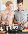 Couple cooking together in a modern kitchen, woman stirring pot on stove, man chopping vegetables on cutting board.